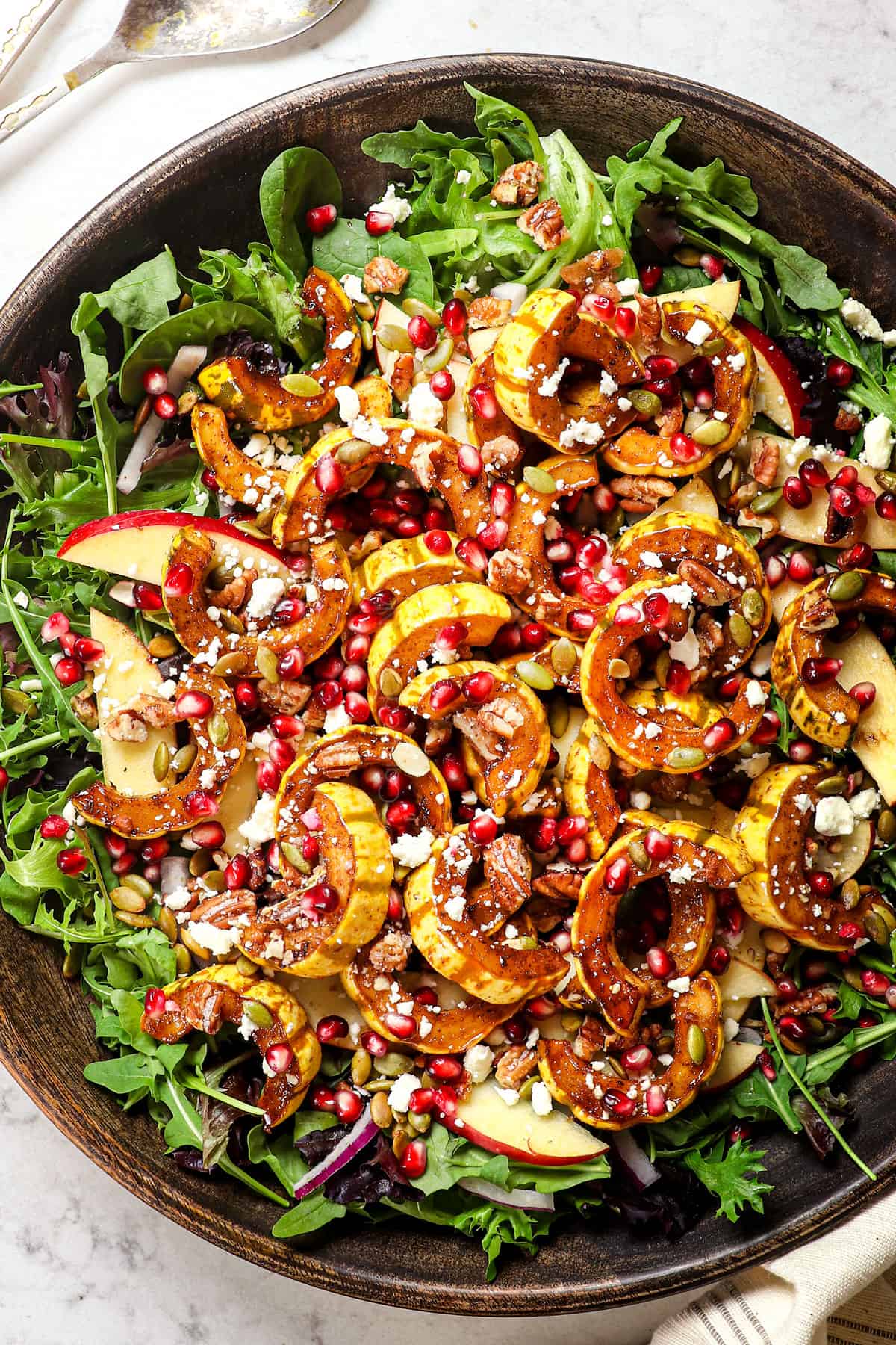 showing how to make squash salad by layering lettuce with red onions, apples, squash, feta, pepitas, and feta