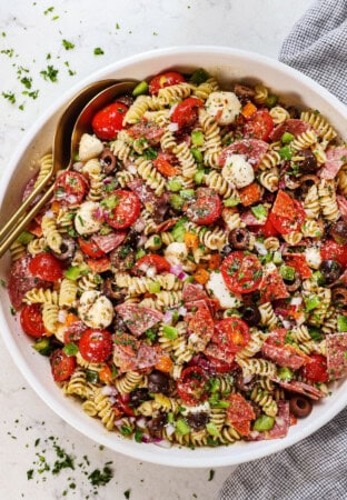 top view of pasta salad recipe in a bowl with salami, tomatoes, bell peppers, olives, pepperoncini, Parmesan and parsley