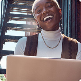 Personne portant un tee-shirt blanc et une veste marron, souriante, en train de tenir un PC