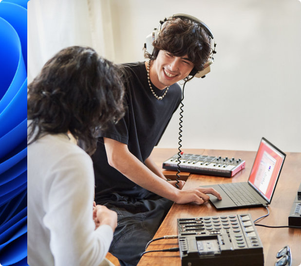 Young man smiling and wearing headphones and another person creating music on a laptop with an electronic keyboard