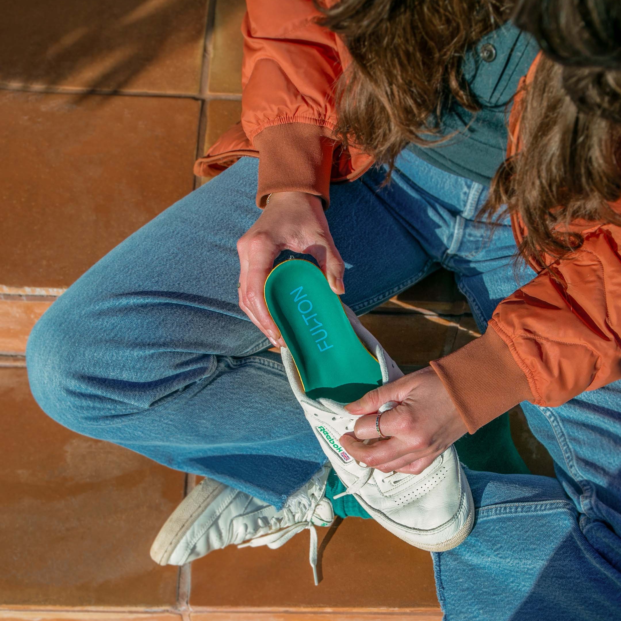 woman in orange jack putting green insole into running shoes