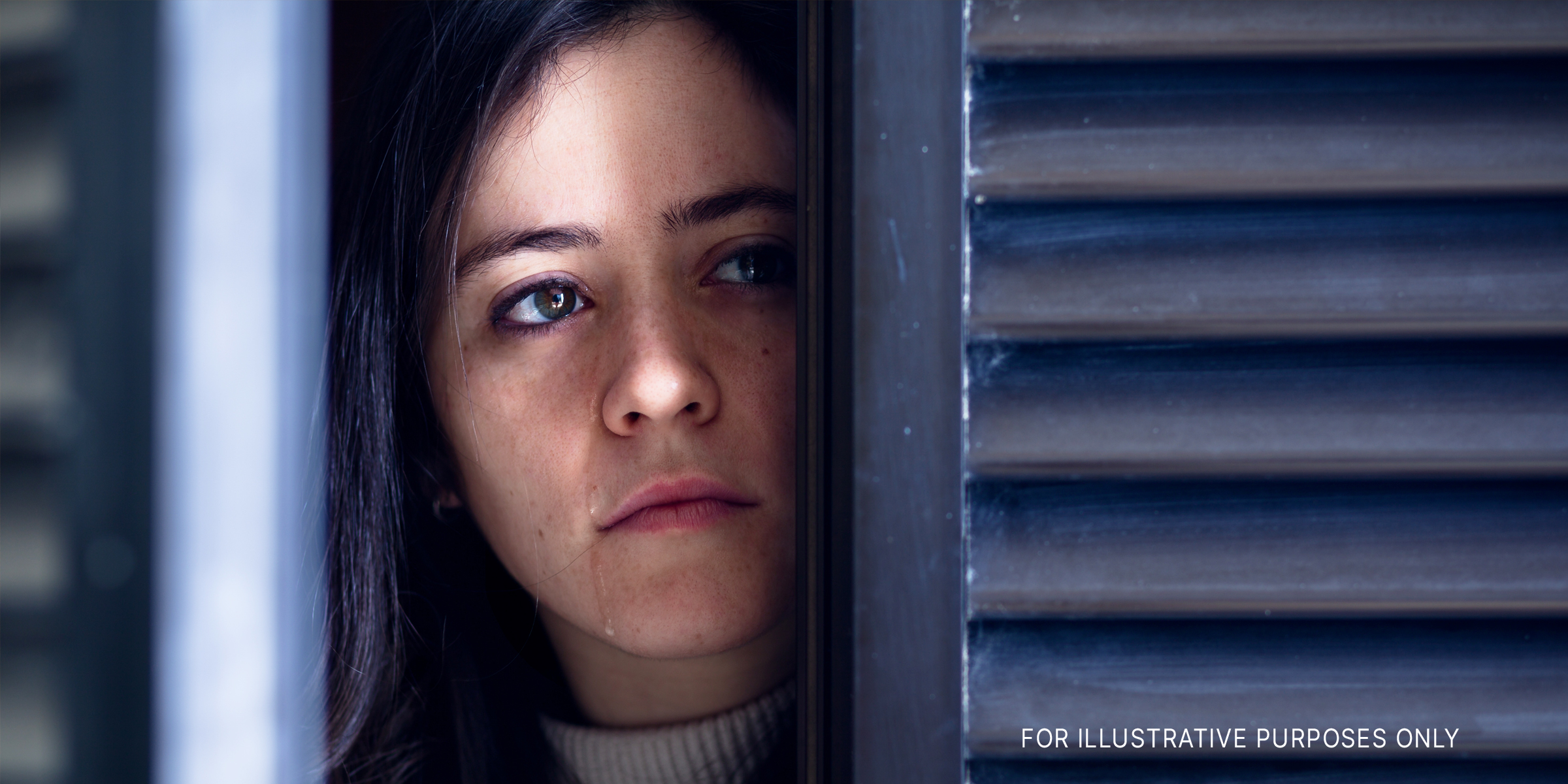 A woman watching through a door/window and crying | Source: Shutterstock