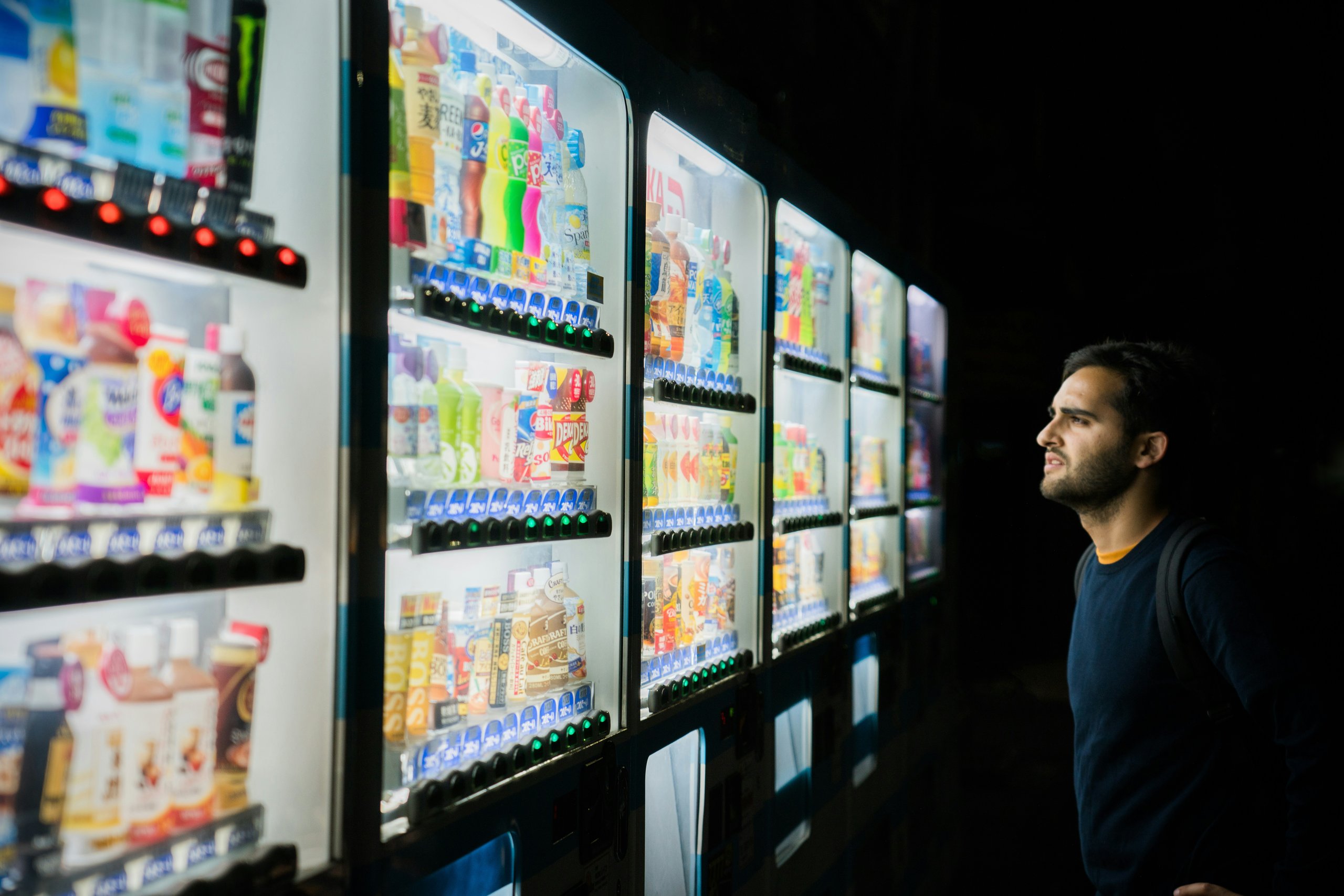 man searching copious fridges full of beverages