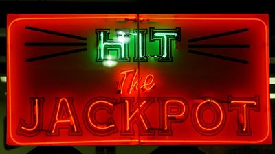 Casino. Gambling. Slots. Slot machine. Luck. Rich. Neon. Hit the Jackpot neon sign lights up casino window.