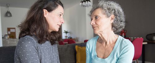 A photo of a serious elderly woman and her daughter talking and holding hands.