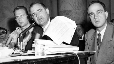 Senator Joseph McCarthy waves a transcript of a monitored call between Pvt. G. David Schine (left) & Secretary of the Army Stevens, Army-McCarthy hearings, June 7, 1954, Washington D.C. Investigation into Communist infiltration of the government. McCarthy. Lawyer Roy Cohn is at right.