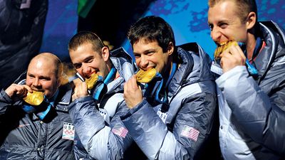 Former U.S. Army World Class Athlete Program bobsledder Steven Holcomb, left, and teammates Justin Olsen, Steve Mesler and Curt Tomasevicz bite their gold medals Saturday night at Whistler Medals Plaza after winning the Olympic four-man bobsled, 2010.