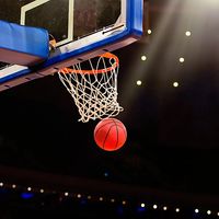 A ball swishes through the net at a basketball game in a professional arena.