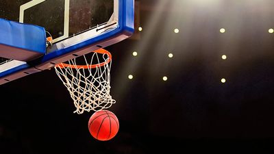 A ball swishes through the net at a basketball game in a professional arena.