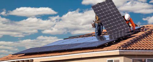 Workers installing solar panels on a house roof.