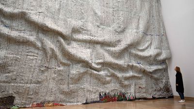 A woman looks the artwork "Rising Sea" of the Ghanaian artist El Anatsui in his exhibition "Triumphant Scala" in the Haus der Kunst in Munich, southern Germany, on April 12, 2019. - The focus of the exhibition is the typical impressive screw-cap work that El Anatsui has made over the past two decades.