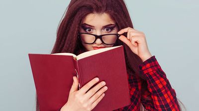 Young woman with glasses reading a book, student