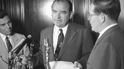 Senator Joseph McCarthy standing at microphone with two other men, probably discussing the Senate Select Committee to Study Censure Charges (Watkins Committee) chaired by Senator Arthur V. Watkins, June 1954