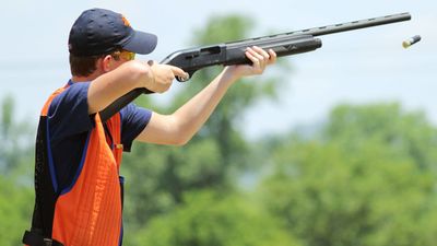 Young man skeet shooting with airborne shell