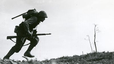 Caption: Through "Death Valley" - one of the Marines of a Leatherneck Company, driving through Japanese machine gun fire while crossing a draw rises from cover for a quick dash forward to another position, Okinawa, 10 May 1945. (World War II)