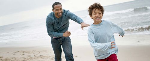 Father chasing son (6-7) on beach.