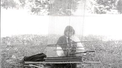 We'wha demonstrates blanket loom weaving on the grounds of the United States National Museum while on a visit to Washington, DC. Zuni hand weaving technique loom