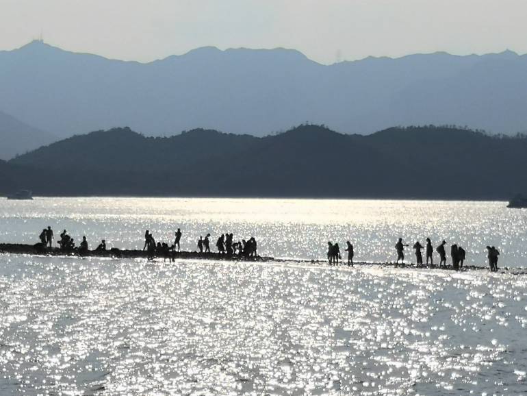 Tourists walking on the Tombolo natural land bridge linking Sharp Island