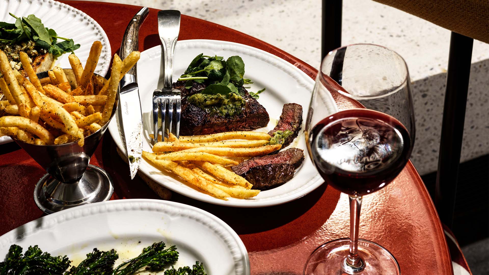 A late of steak frites on a deep red table with a glass of wine