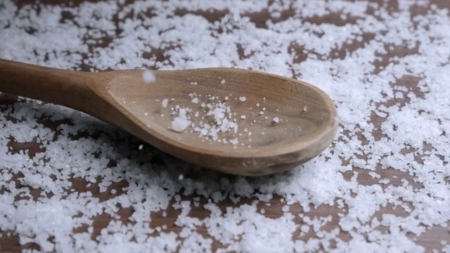 White salt falls on a wooden spoon