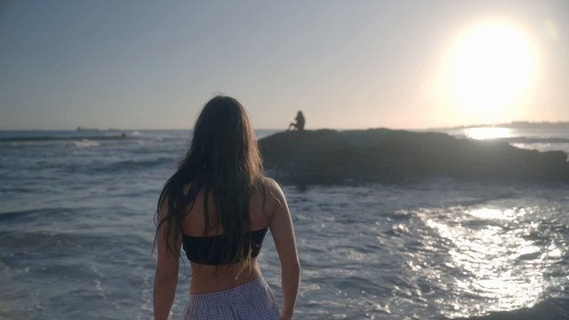 Woman Waving to Photographer on a Rock at the Beach