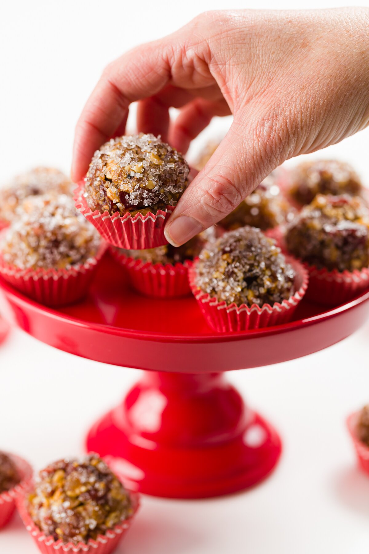 Sugar plums in red mini cupcake liners on a red cupcake stand with a hand selecting one