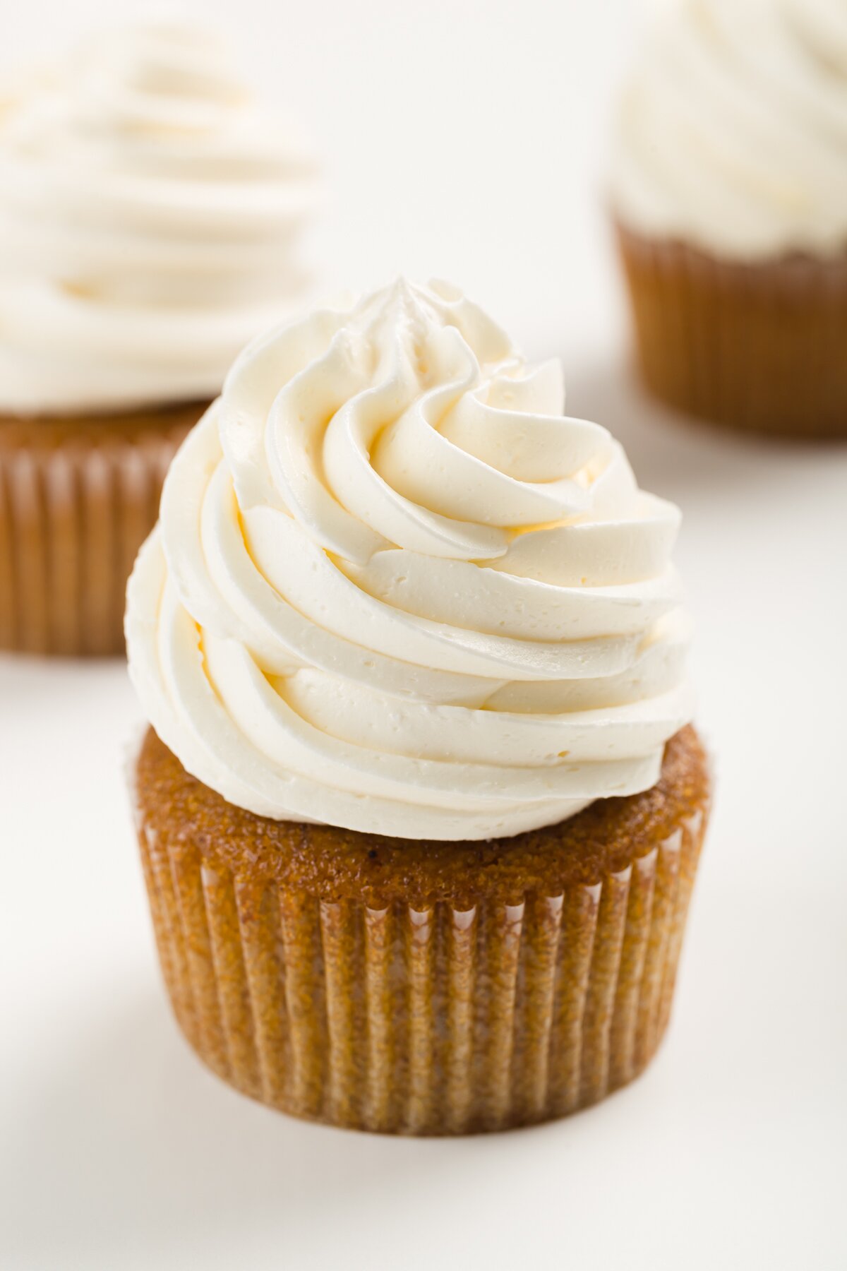 tight shot of a cupcake frosted with Italian meringue buttercream frosting with several others behind it