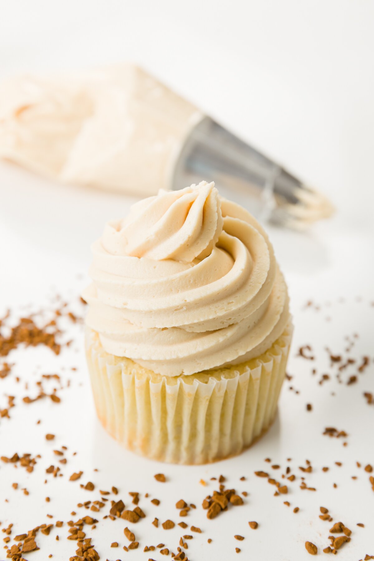 cupcake topped with coffee frosting and a piping bag in the background