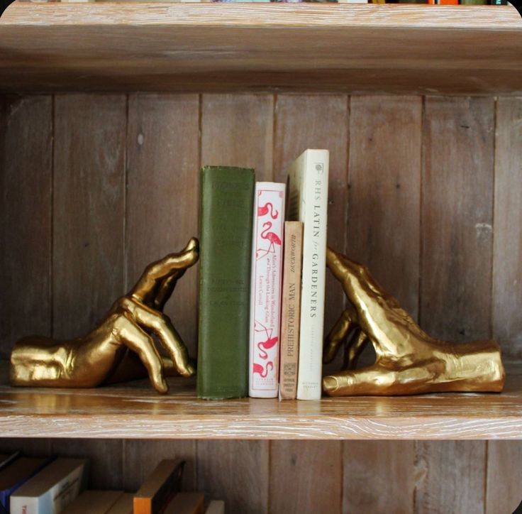 Hand bookends holding up four books on a shelf.