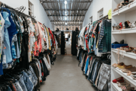 A photo of a long thrift store with clothing racks on either wall.