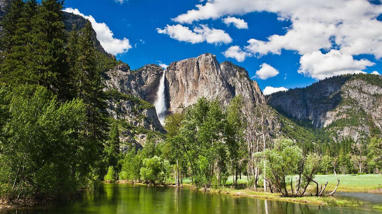 A lake next to trees and a rocky hill with a waterfall flowing down it