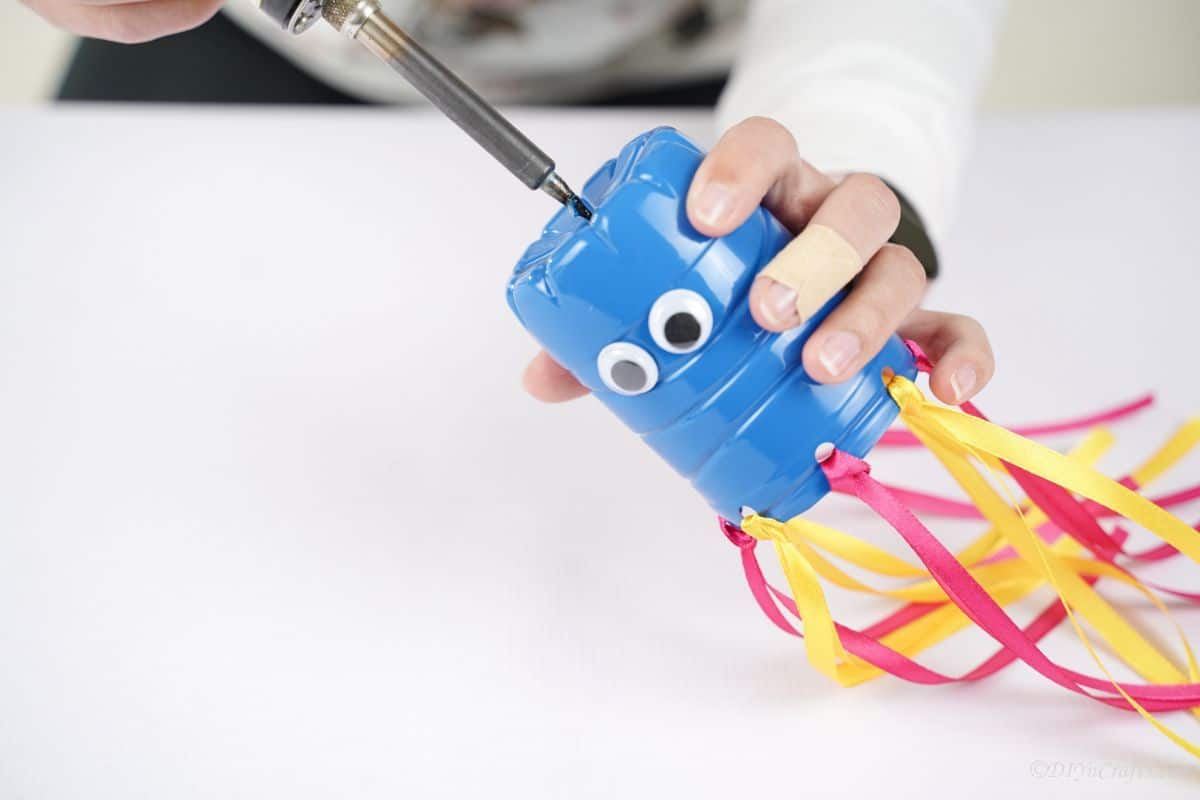 soldering gun held above blue plastic bottle