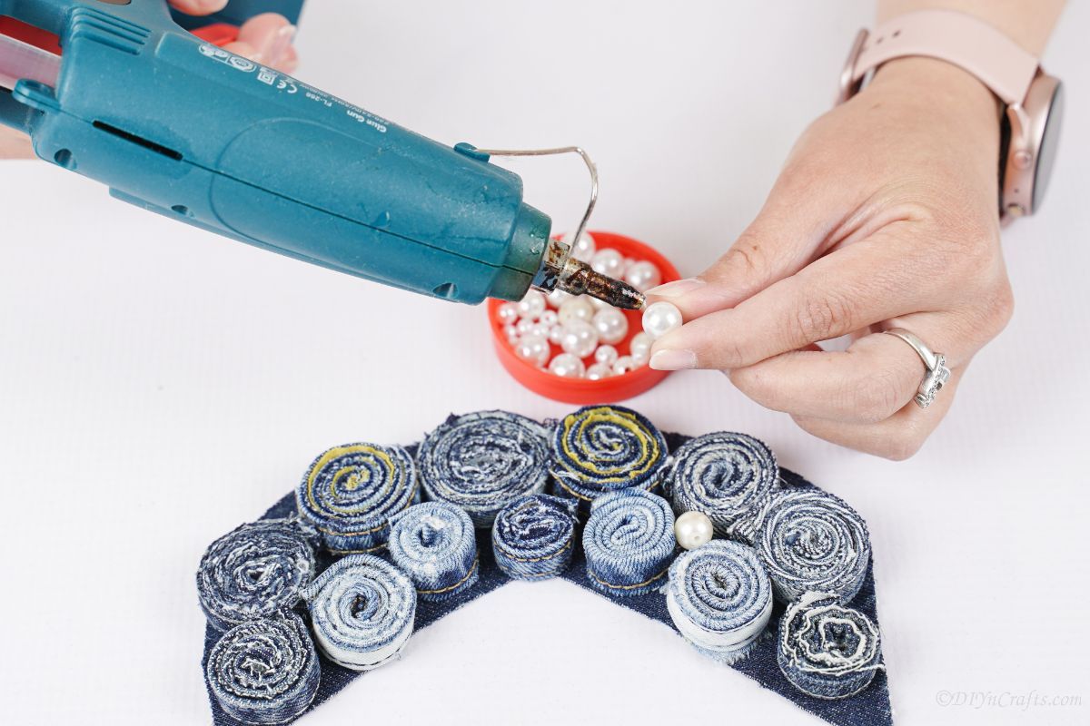 hand adding glue to pearl bead above denim necklace base