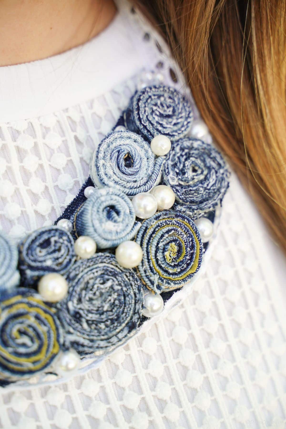 side of denim necklace laying against collar of white shirt on brunette