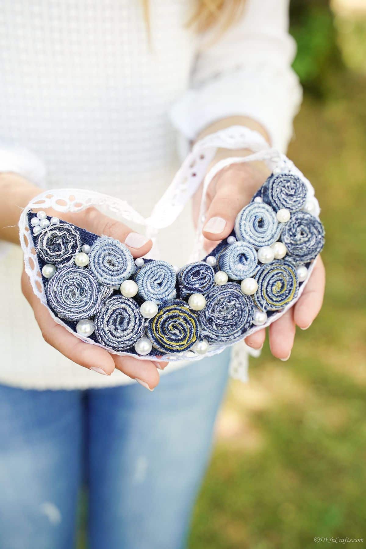 woman in white shirt and jeans holding denim necklace