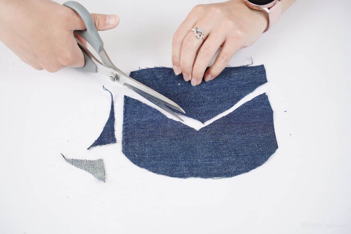 hand holding gray scissors cutting a piece of denim