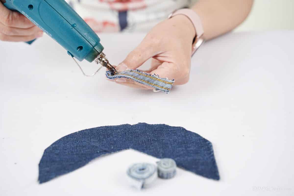 hand holding a denim seam and a glue gun