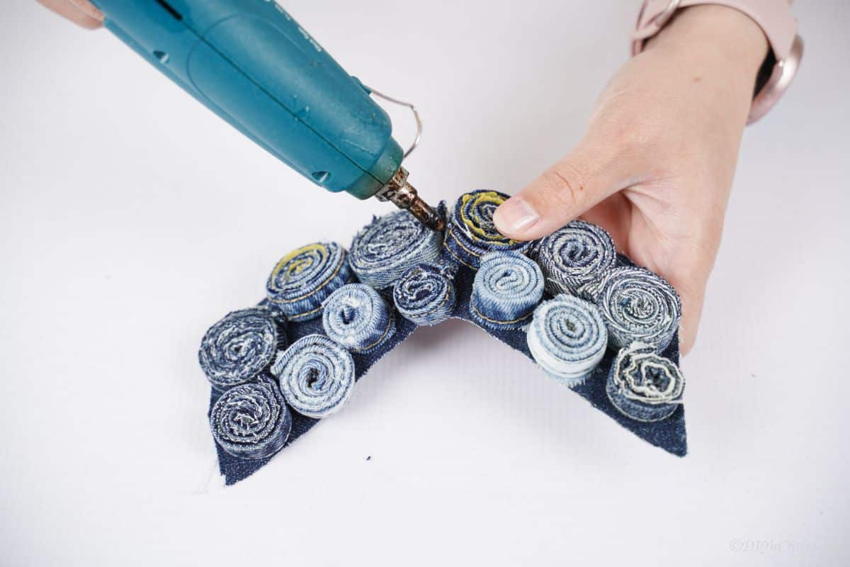 hand holding blue glue gun to glue denim rolls onto base