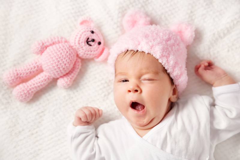 Cute newborn baby girl lying in the bed on white blanket with pink teddy