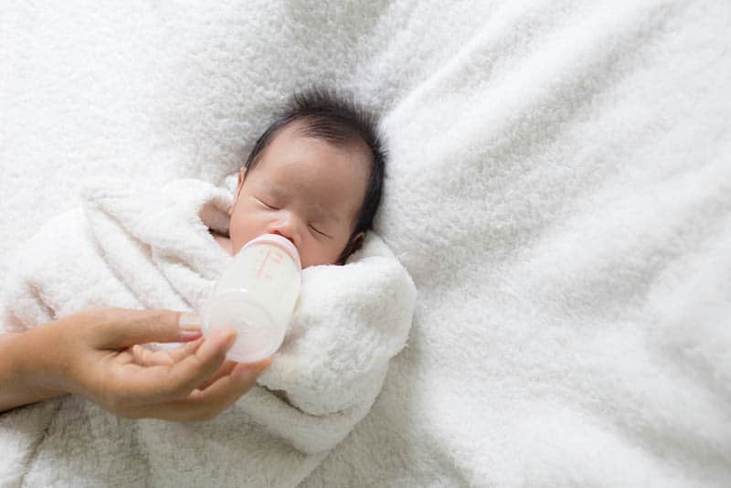 mother feeding her newborn baby with milk bottle on the bed