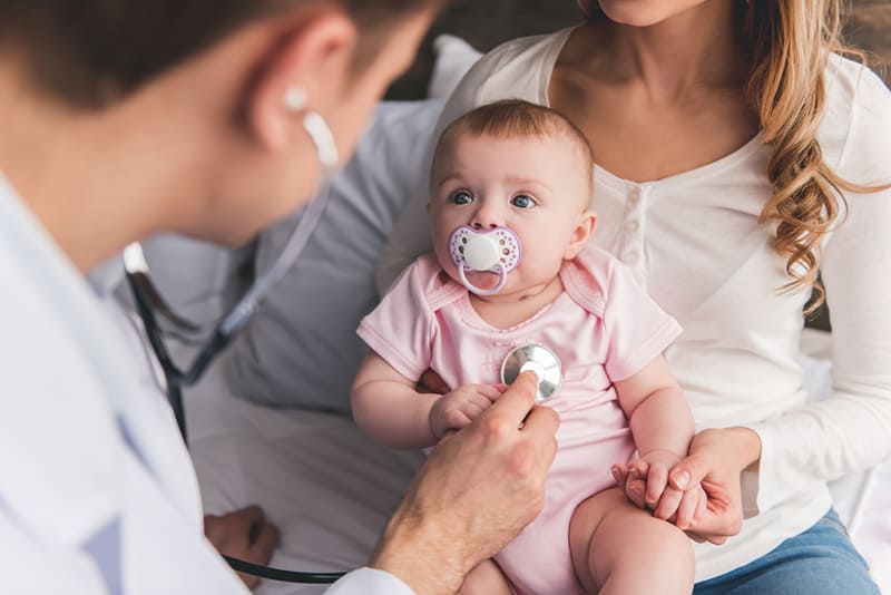 young mother holding her baby girl while doctor examining her