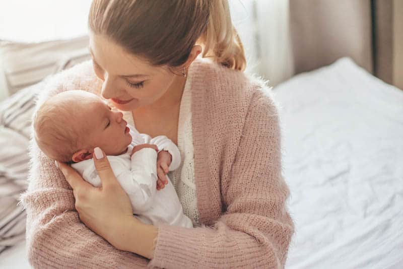 young mother holding newborn baby on bed