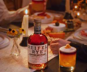 A person holding a glass of whisky with a bottle of Reifel Rye