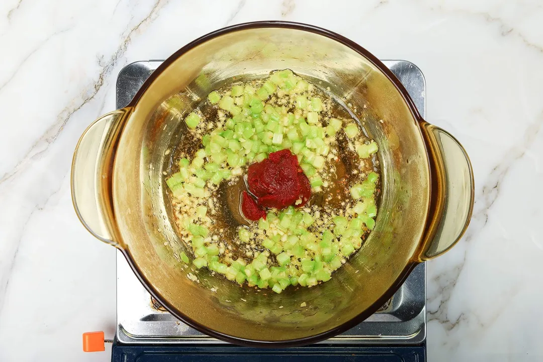 A saucepan cooking diced vegetables with some tomato paste in the center.