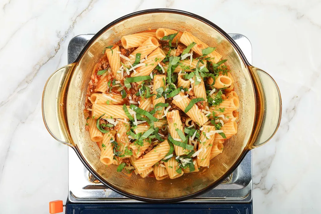 A saucepan cooking tortiglioni pasta with some fresh herbs sprinkled over.