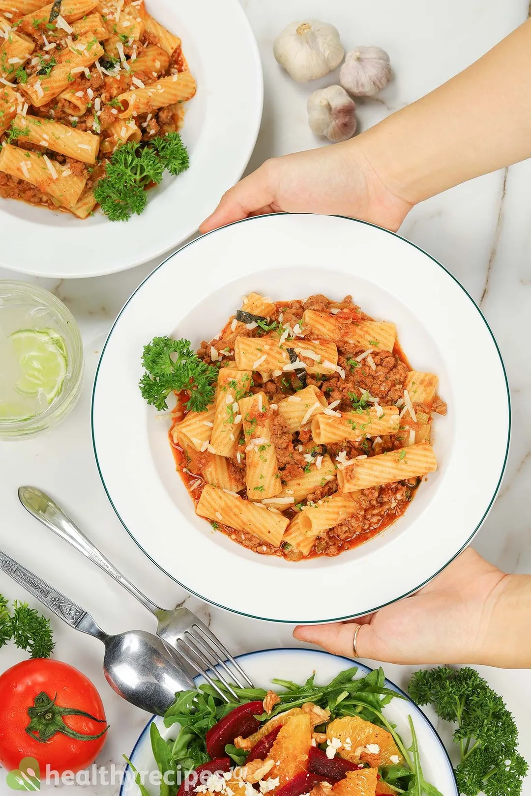 Two hands holding up a plate of Pasta Bolognese