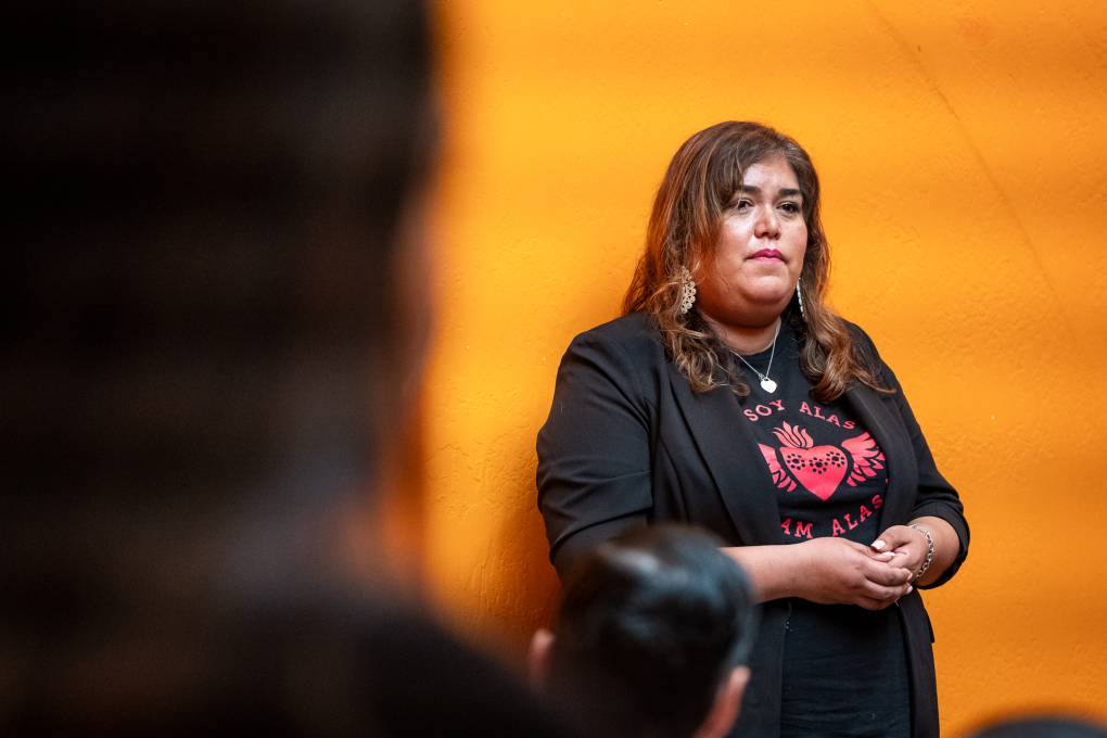 A person with long hair stands in front of a group of people in a room painted bright orange.