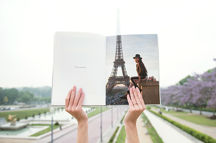 Woman in Paris holds up Portrait Photo Book to align picture with Eiffel Tower