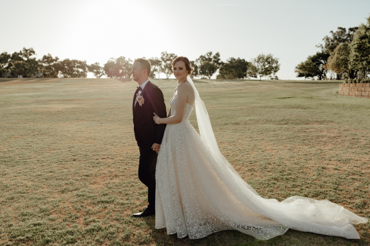 Bride and groom walking together, the bride wears a sparkly white strapless A-Line wedding dress with a long train