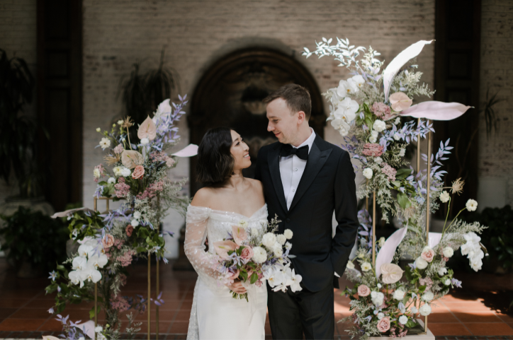 Bride and groom look at each other smiling at flower arch at the wedding aisle